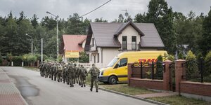 Uniformierte marschieren auf einer Straße in einer Kleinstadt