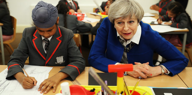 Theresa May sitzt neben einer Schülerin, die zeichnet
