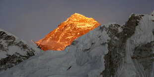 Von Sonne angestrahlter Gipfel, davor schneebedeckte Berge im Schatten