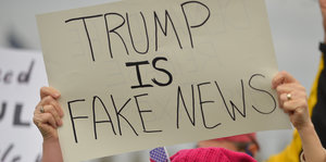 Eine Demonstrantin hält ein Schild hoch auf dem steht: "Trump is Fake News"