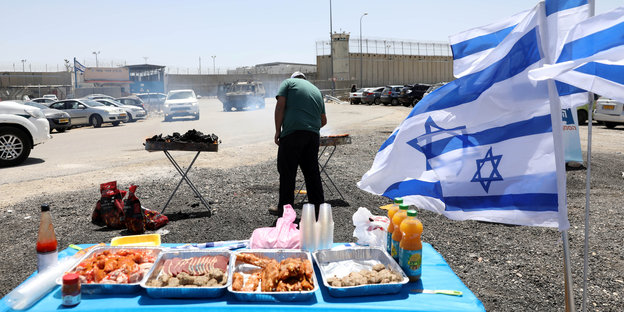 Vor einem Gefängnis in Israel grillt ein Mann neben israelischen Flaggen