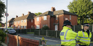 Zwei Polizisten in gelben Warnjacken stehen in einer ruhig wirkenden britischen Nachbarschaft