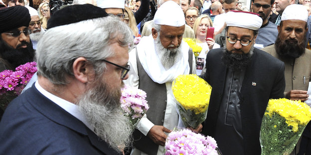 Juden, Christen und Muslime stehen zusammen, sie halten Blumen in den Händen
