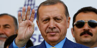 Erdogan hebt die rechte Hand hinter ihm steht ein Mann mit Sonnenbrille