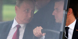 Putin und Macron sitzen in einem Golfcart, durch die trübe Scheibe sieht man, wie Putin Macron prüfend anguckt