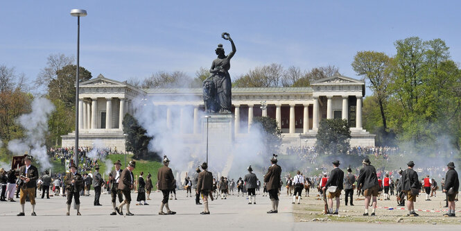 Bayern in Lederhosen stehen versprengt auf der Theresienwiese und schauen hoch zur Statue der Bavaria