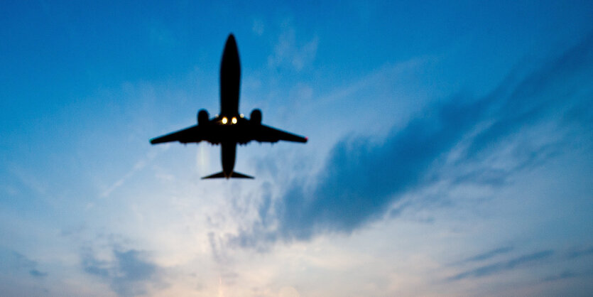 Ein Flugzeug steigt in der Dämmerung vor stahlblauem Himmel auf