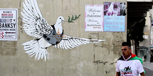 Ein Marathonläufer läuft an einer Wand mit Plakaten vorbei: "Welcome to Palestine" und eine Friedenstaube im Visier