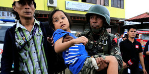 Ein Soldat trägt ein Kind, ein Mann läuft neben ihnen