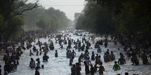 Viele Menschen stehen bei offensichtlich großer Hitze in einem breiten Fluß