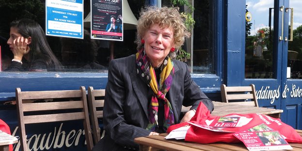 Eine Frau mit Locken und buntem Schal sitzt vor einem Café