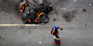 EIn Mensch läuft neben einem brennenden Motorrad