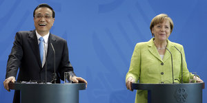 Li Keqiang (li.) und Angela Merkel stehen an Pulten vor blaum Hintergrund