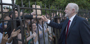 Ein Mann, Jeremy Corbyn, grüßt Menschen hinter einem Zaun