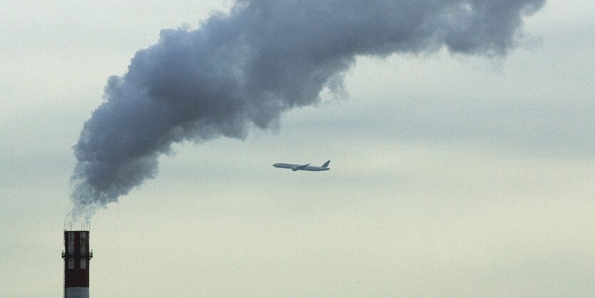 Aus einem Schornstein steigt Qualm auf, dahinter fliegt ein Flugzeug