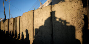 eine Mauer, darauf der Schatten eines Bewaffneten