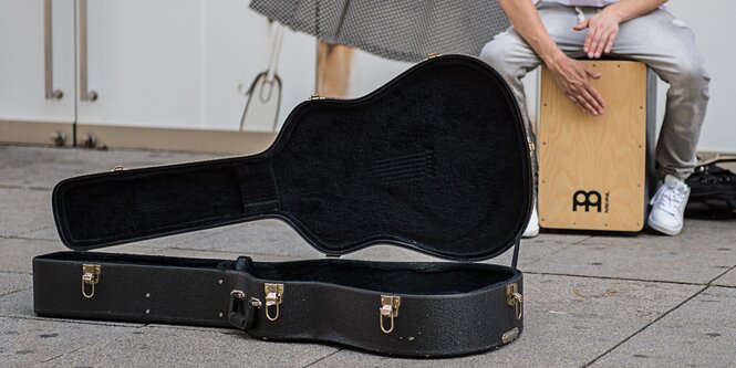 Ein Gitarrenkoffer liegt aufgeklappt vor einem Straßenmusiker