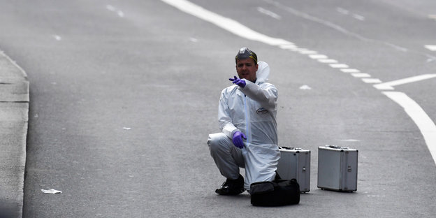 Ein Mann in weißer Schutzkleidung kniet auf der Straße