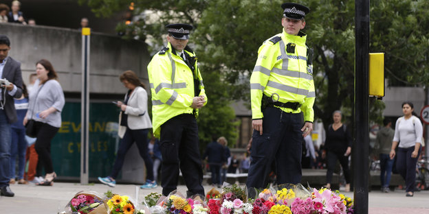 Polizisten stehen vor Blumen auf einer Straße