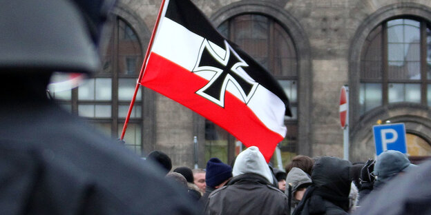 Neonazis schwenken hinter einer Polizeikette eine Fahne in Dresden