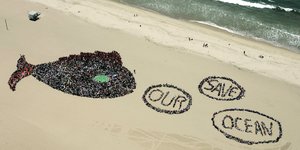 Menschen am Strand formen einen Fisch mit drei Luftblasen, in denen "Save our ocean" steht