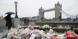 Eine Frau mit Regenschirm steht vor den Blumen, die für die Opfer des Anschlags vor der London Bridge niedergelegt sind
