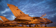 Drei Bundeswehr-Tornados stehen im rötlichen Lich von Scheinwerfern auf einem Rollfeld vor dunkel bewölktem Himmel