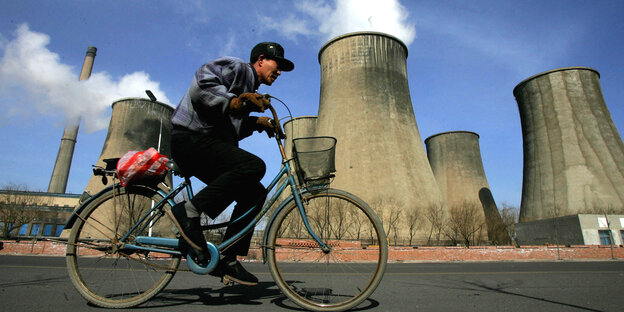 Ein Chinese fährt auf einem Fahrrad an einem Kohlekraftwerk vorbei