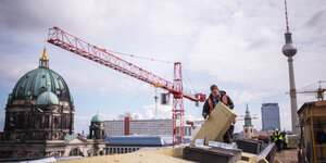 Ein Bauarbeiter arbeitet auf dem Dach, im Hintergrund Berliner Dom, Fernsehturm und ein Baukran