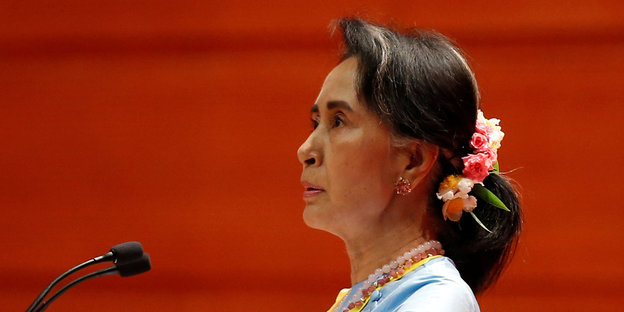 Myanmars Regierungschefin Aung San Suu Kyi ist im Profil vor rotem Hintergrund zu sehen, sie guckt ernst