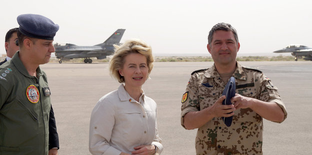 Ursula von der Leyen steht zwischen einem jordanischen Kommandanten und einem Bundeswehr-Oberst auf einem Rollfeld
