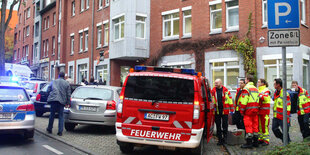 Ein Feuerwehrauto und mehrere Feuerwehrleute und andere Menschen stehen vor Reihenhäusern