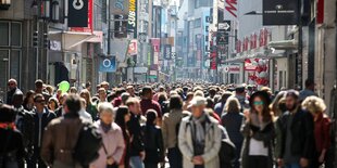 Man sieht eine Fußgängerzone mit ganz vielen Menschen. An den Seiten sieht man die Markennamen verschiedener bekannter Shops.