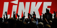 Menschen heben vor einem risigen Logo der Linkspartei Hände mit Zetteln hoch