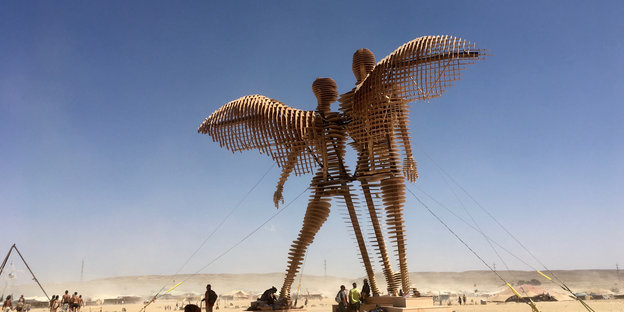 Zwei überlebensgroße Skulpturen aus Holz stehen in der Wüste