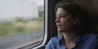 Eine Frau sitzt im Zug und sieht aus dem Fenster.