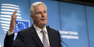 Ein Mann steht gestikulierend vor einem Banner mit dem EU-Logo