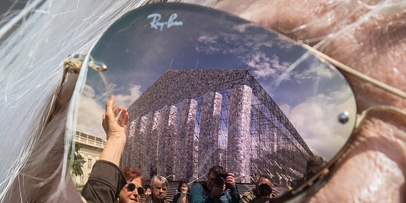 Im Glas einer verspiegelten Sonnenbrille spiegelt sich ein Tempel aus Büchern