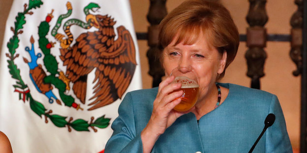 Angela Merkel hebt ein Glas Bier zum Mund.