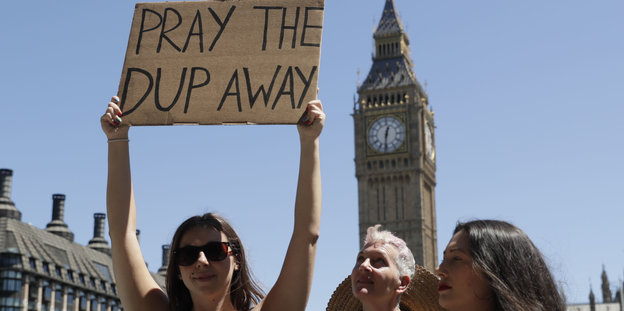 Jemand hält ein Schild hoch, auf dem steht: "Pray the DUP away"
