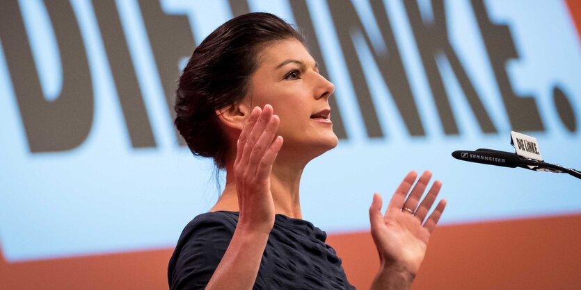 Sarah Wagenknecht mit ausgebreiteten Armen an einem Rednerpult