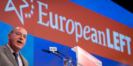 Kahler Mann mit Brille, es ist Gregor Gysi, am Rednerpult, hinter ihm die Aufschrift "European Left"