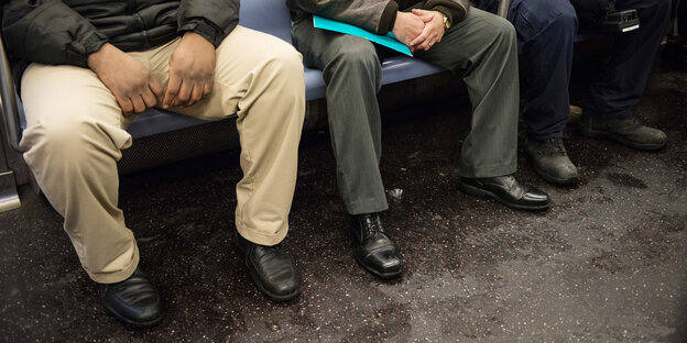 Personen sitzen breitbeinig in der U-Bahn