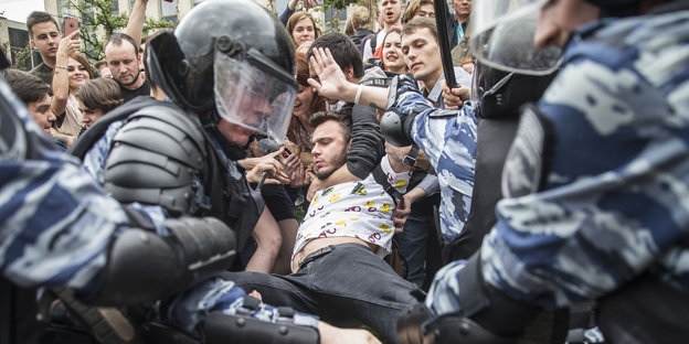 Polizisten zerren an einem Demonstranten, hinter dem andere Demonstranten stehen