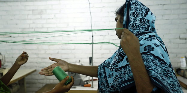 Eine Frau mit Kopftuch hält eine Schnur in der Hand. Sie arbeitet in der Textilproduktion.