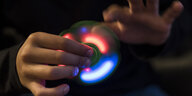 Eine Hand hält einen Fidget Spinner mit LED-Licht, die andere Hand stößt ihn an