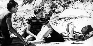 Eine schwarz-weiß Aufnahme aus einem Film, eine Frau und zwei Männer am Strand