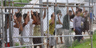 Menschen stehen hinter einem Gitterzaun