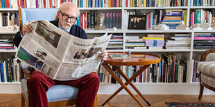 Mann mit Zeitung auf Sessel vor Bücherwand