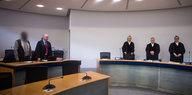 Ein Angeklagter und sein Anwalt stehen in einem Gerichtssaal,, im Hintergrund drei Richter
